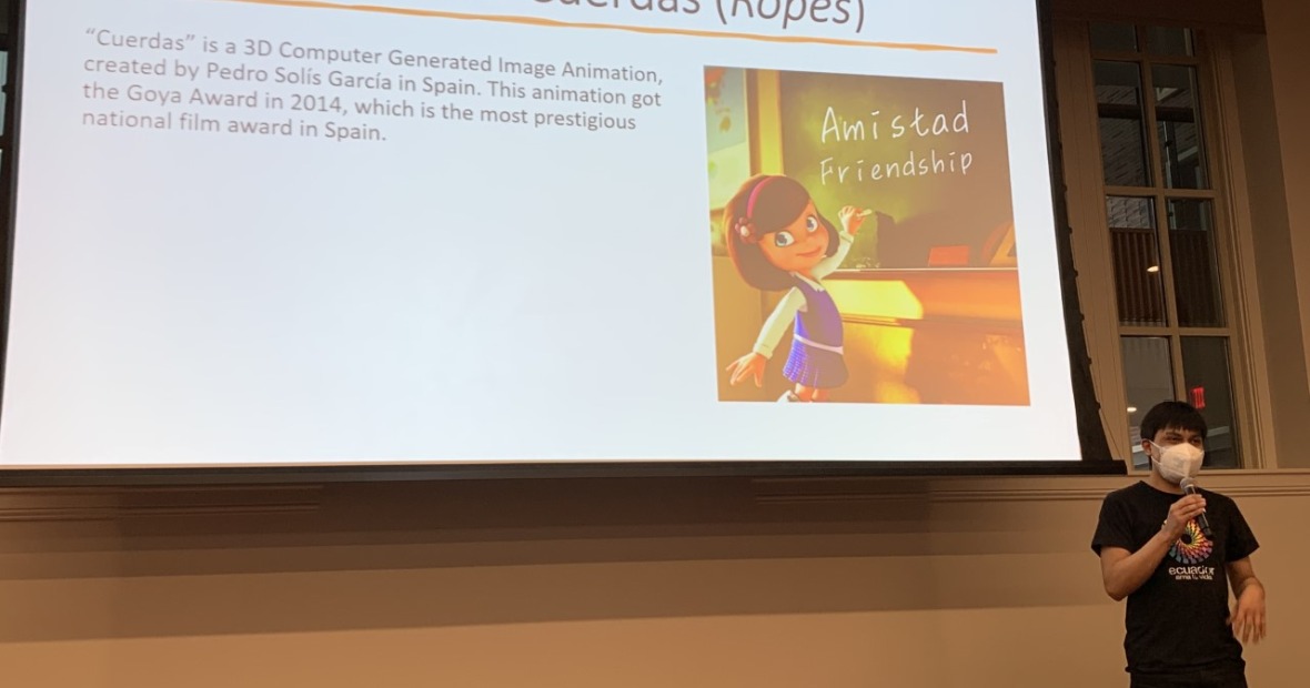 Student speaking beneath a screen showing infor about Spanish cartoon Cuerdas (Ropes)