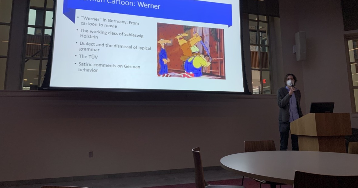 Student speaking beneath as screen showing information about German cartoon Werner