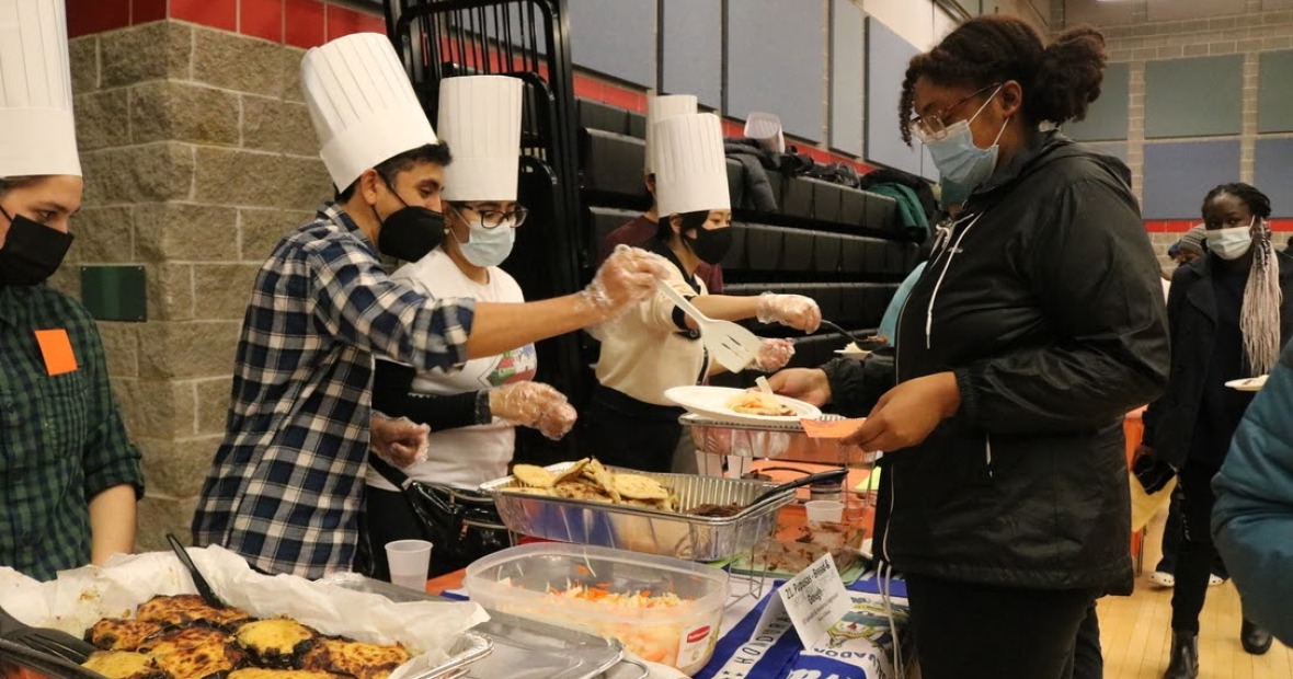 ISO Food Bazaar 2021with students in chef's toques serve others passing in a line