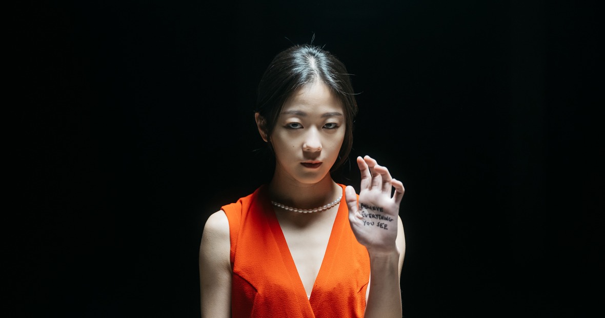 A young woman in an orange dress holds up her hand, which has writing on the palm