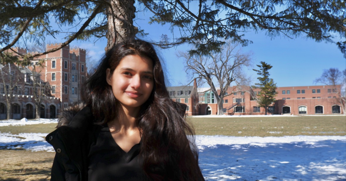 Ekta standing next to a tree in a snowy field with buildings behind her