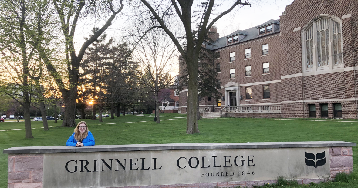 MJ Uzzi poses with the Grinnell College sign at sunrise