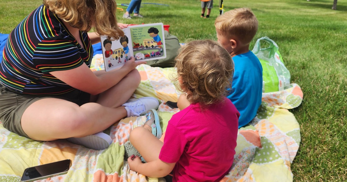 college student reading to two young children outside 