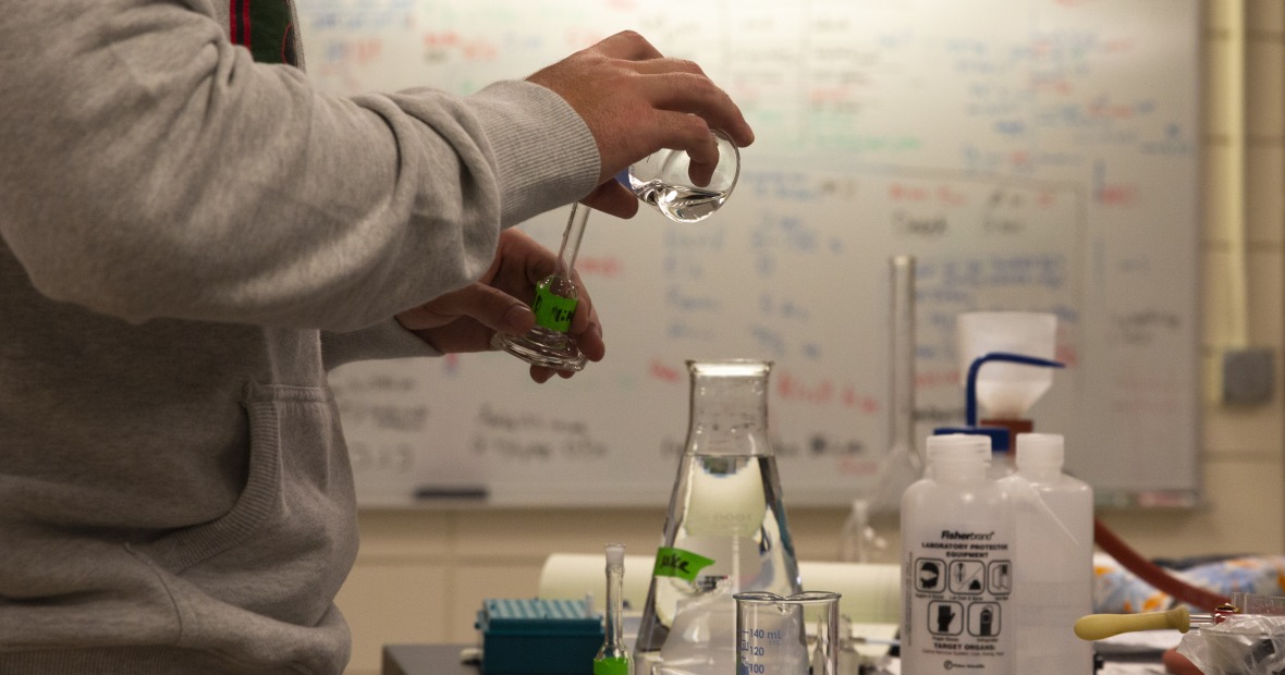 A student pours a solution from a flask into a test vial.