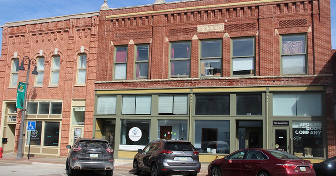 A brick and stone facade with Beyers carved on a plaque over the 2nd story windows houses a few businesses behind large windows on the first