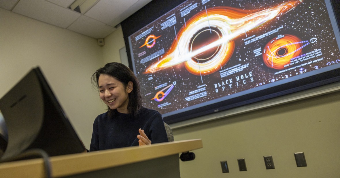 Lotus Liu ’27 presenting her research on black hole shadows. A projection of black hole concept images displays behind her.