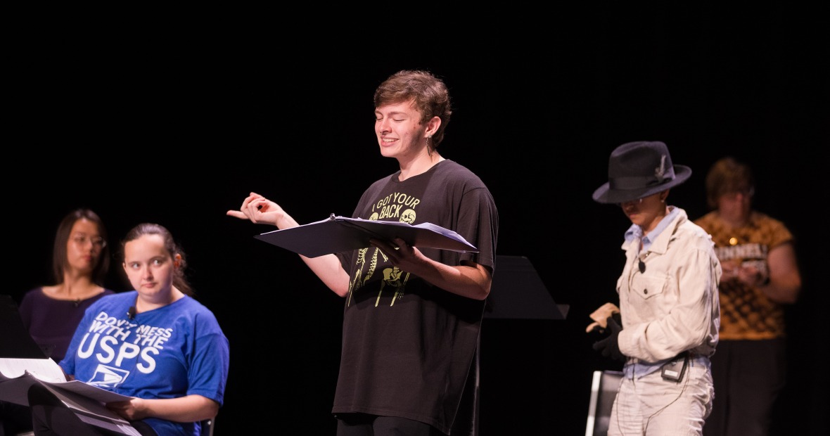 Five students on a dark stage holding black binders