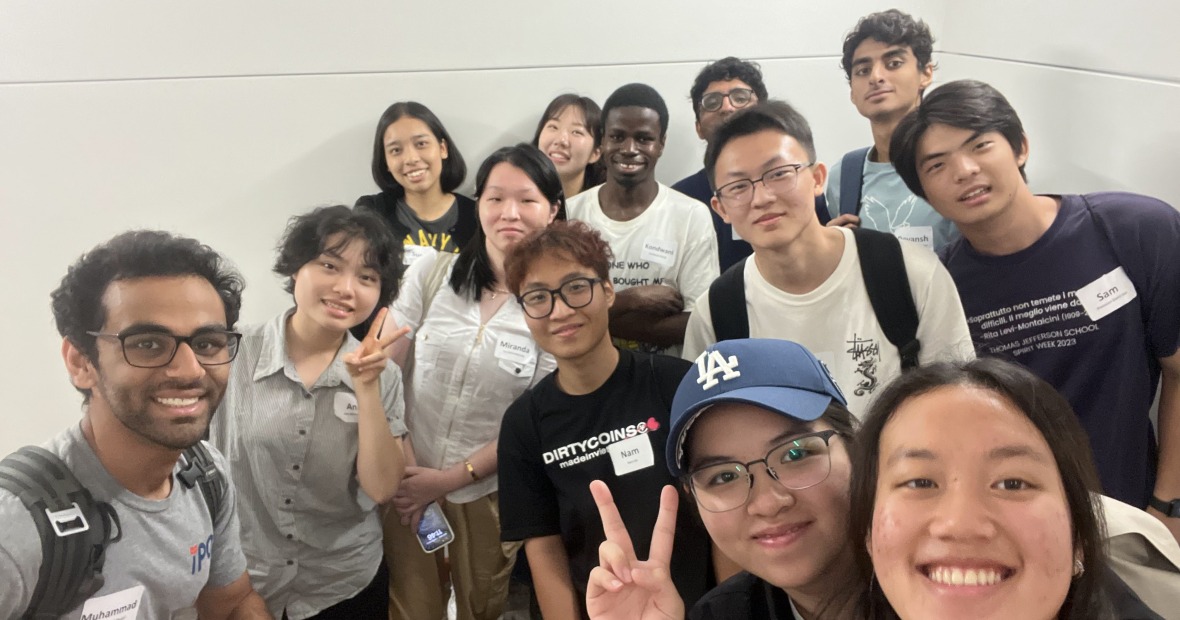 A large group of students stand together in a hallway and smile at the viewer