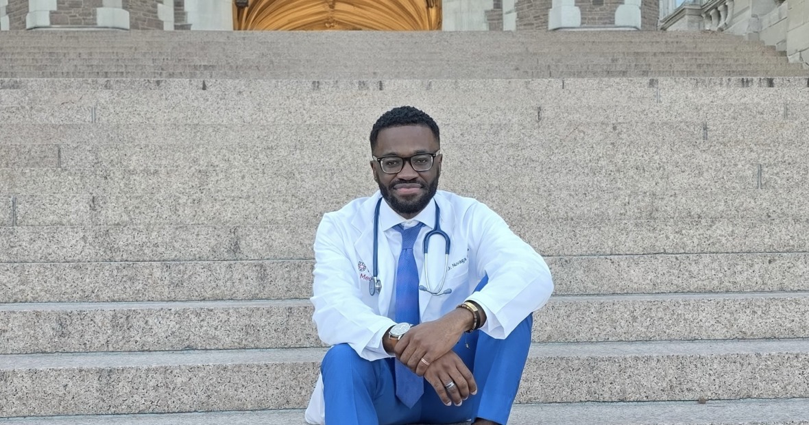 MJ Ketcha wearing a white medical coat and sitting on stone steps.