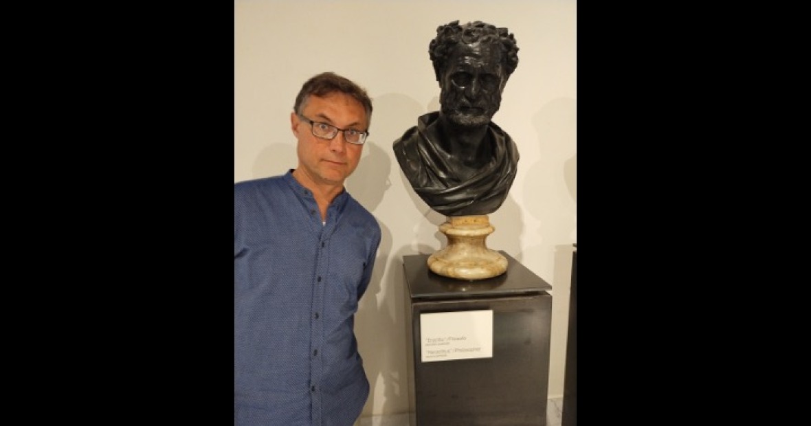 Professor Joe Neisser standing next to a black stone bust