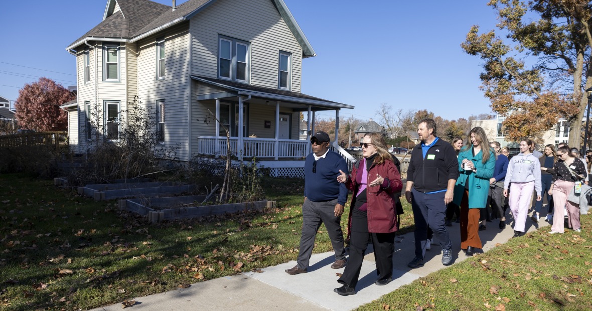 Susan Sanning leading a group of adults walking down the sidewalk past a white house.