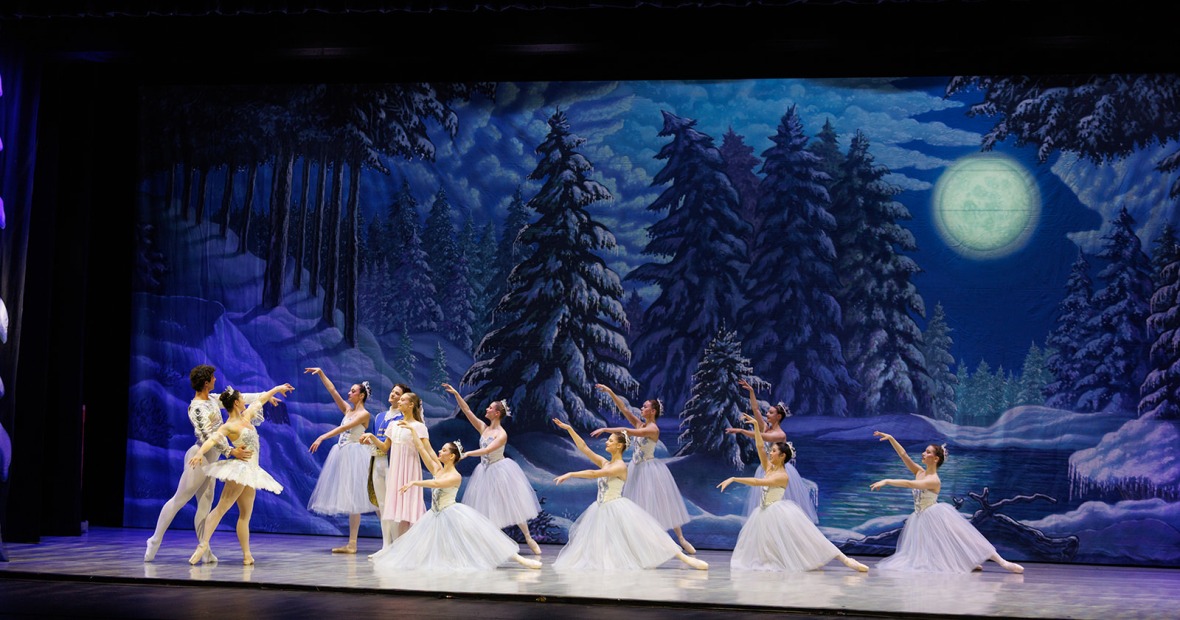 dark snow scene on stage with a man and a woman in white dancing ballet
