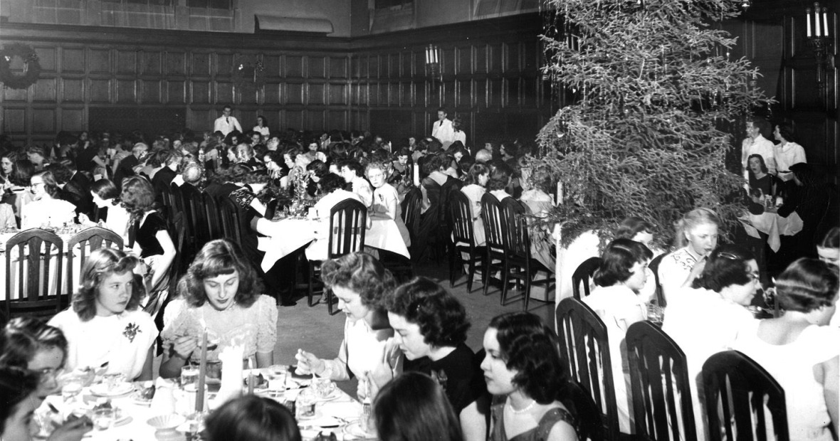 Black and white vintage photo showing women in long dresses enjoying a dinner in Main Hall under a huge Christmas tree