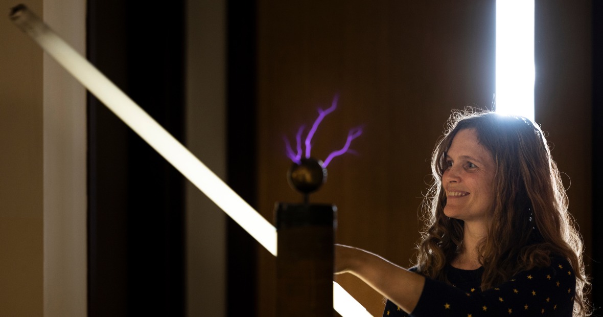 Charlotte Christensen holding a long cylindrical light with a metal sphere emitting purple cracks of light sits in front