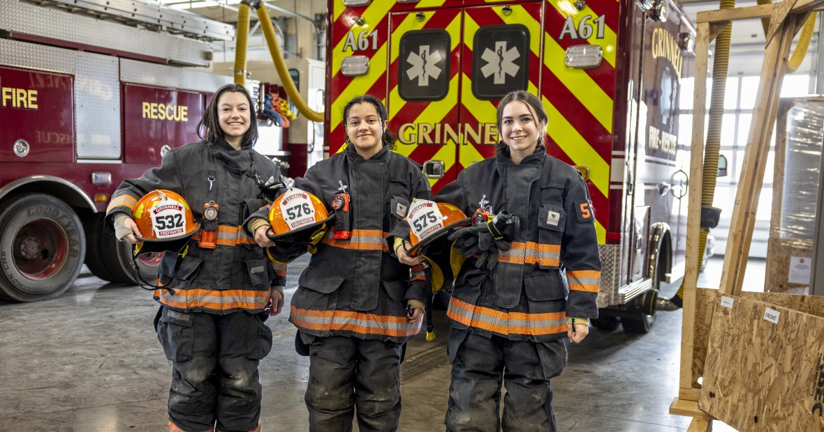 Three students with fire equipment on and ambulance behind them. 