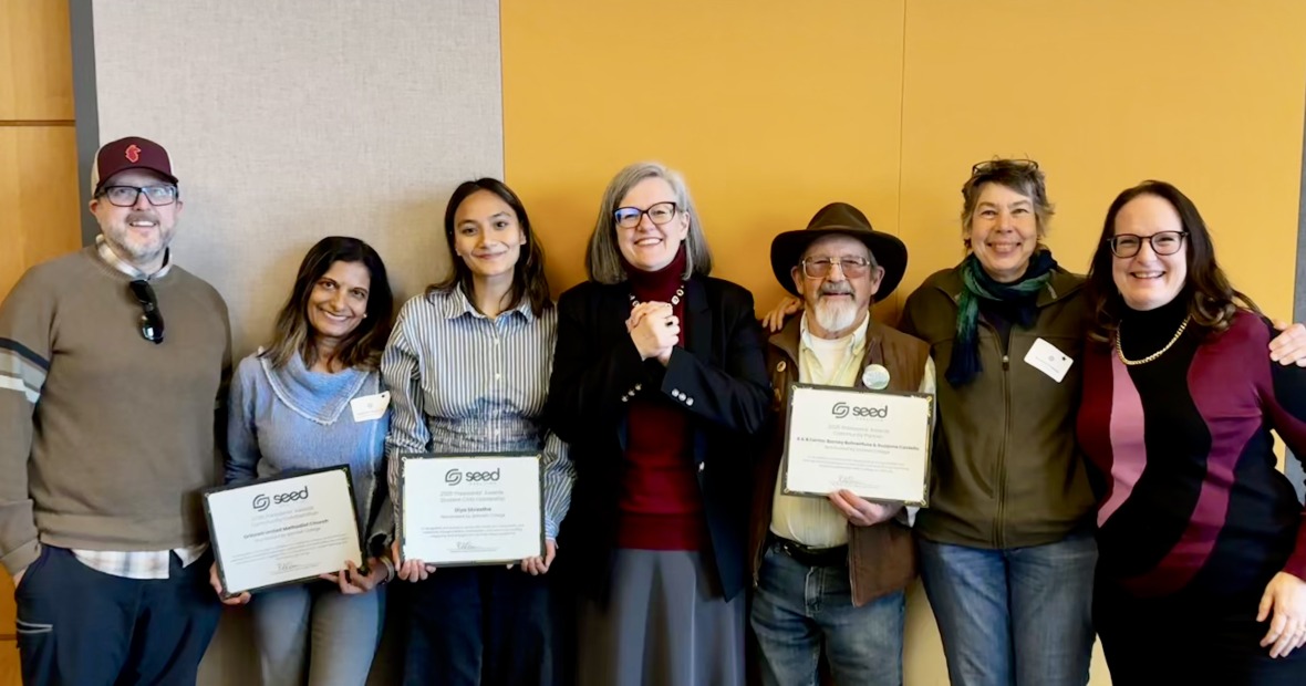 Seven people standing in a line, three holding certificates