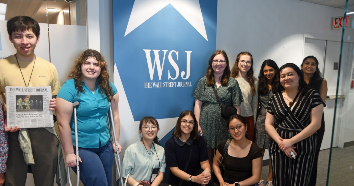 Ten students posing around a blue and white sign that reads "WSJ Wall Street Journal"