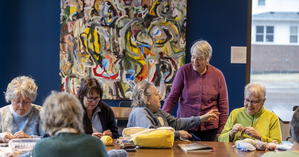 Six older women sitting around a table and knitting