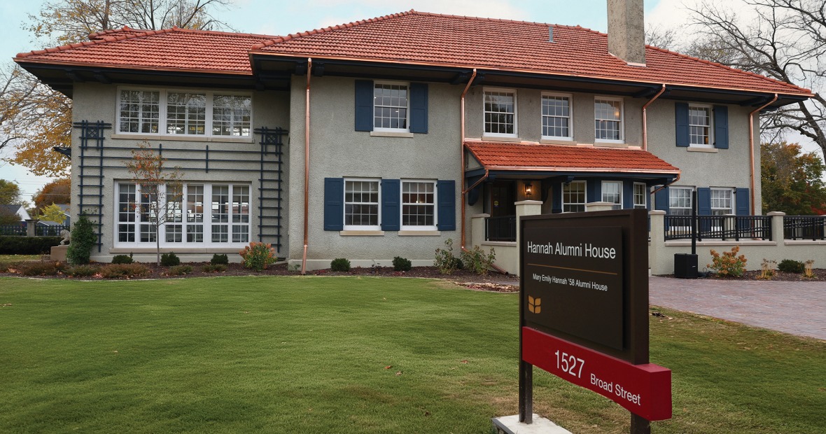 A two story stucco house with a red tile roof has a sign proclaiming it Hannah Alumni House 1527 Broad St