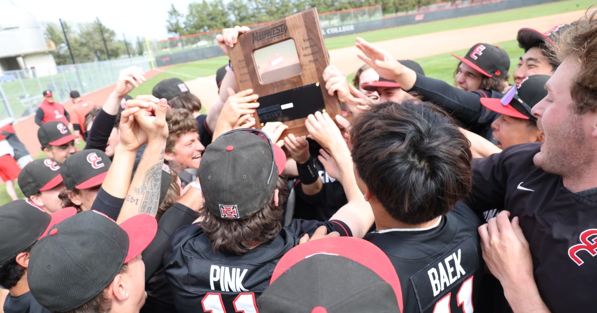 Baseball players wearing black uniforms with red accents celebrate in a group holding a wooden plaque