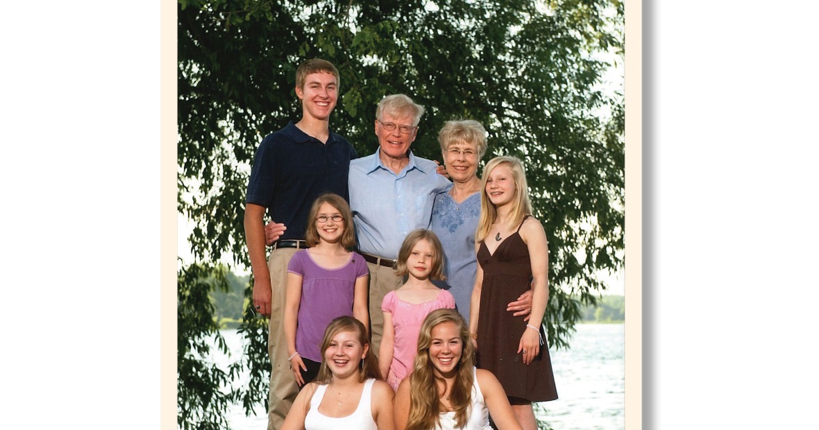 George and Sue Drake pose with their grandchildren in front of a lake on a sunny day. 