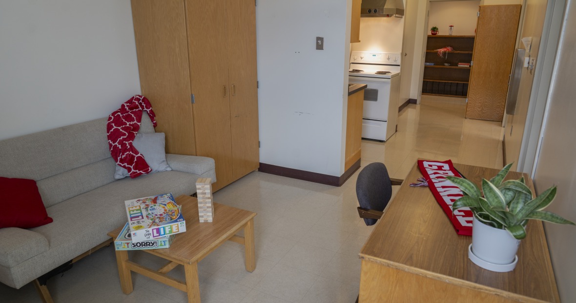 An apartment living room connected to a kitchen. Furnitue includes a couch and TV stand.