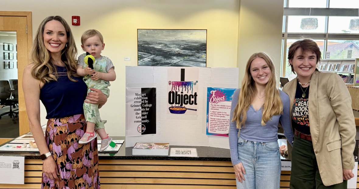 A woman holding a young child stands on the left of a poster board reading "I Object" and two students stand together on the right