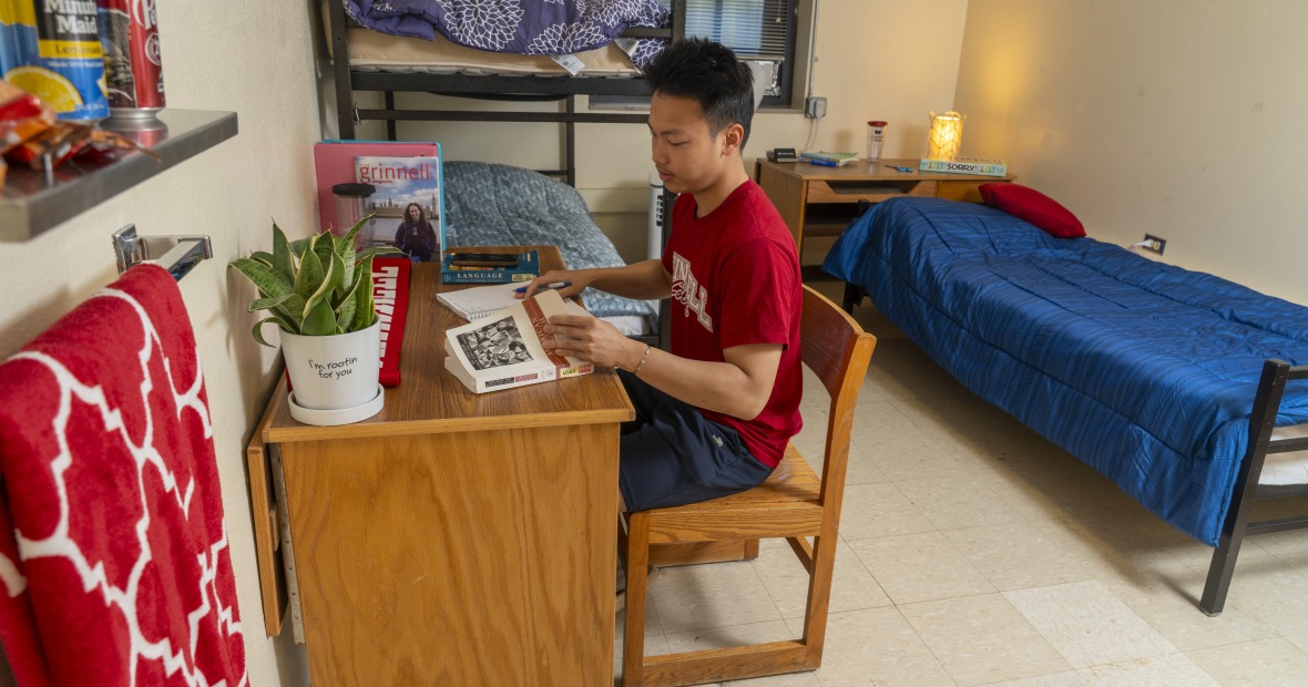 Student at a desk in a single bedroom with a window and bed.