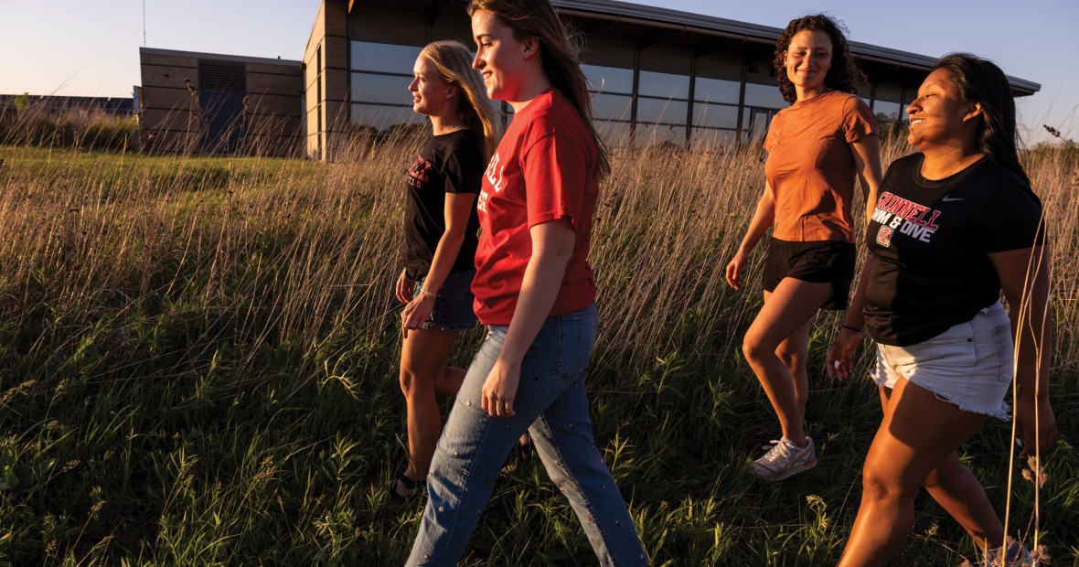Four women walk in front of a research facility located behind prairie grasses