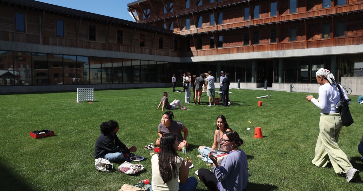 A diverse group of students sits and stands in small groups among lawn games in a grassy courtyard of a residence Hall 