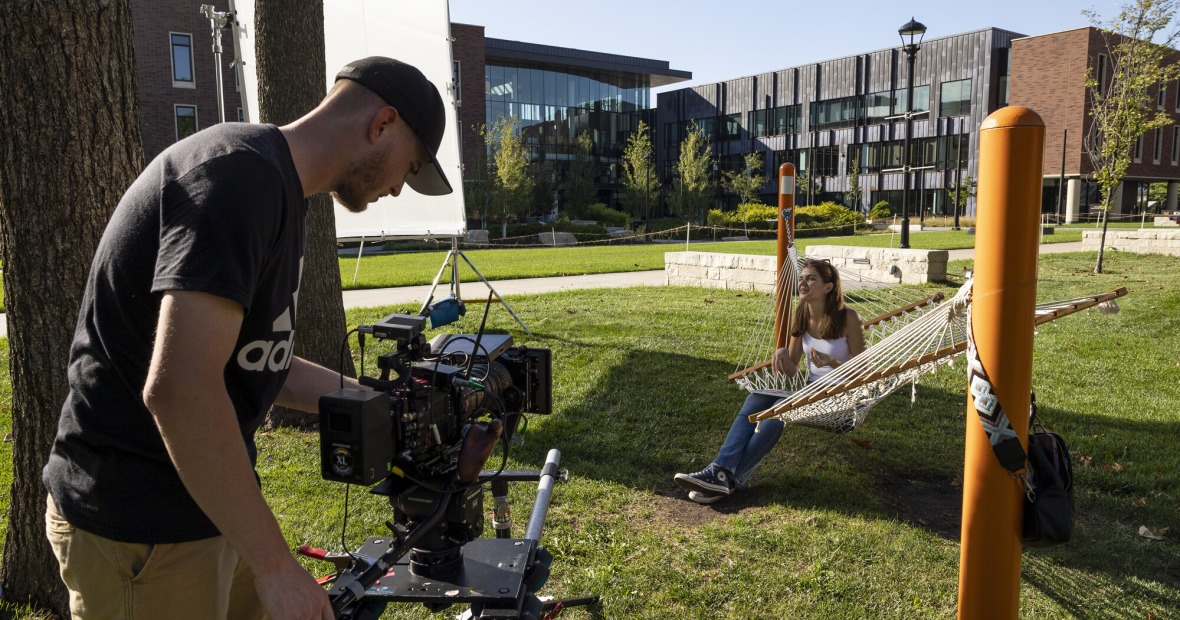 man with a video camera on campus with girl in hammock