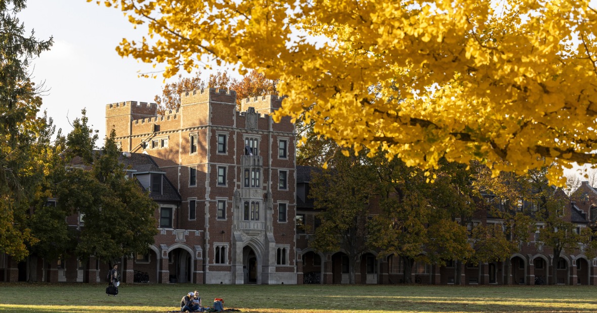 Students lying on Mac Field in front of Gates Tower with tree branches in the foreground.