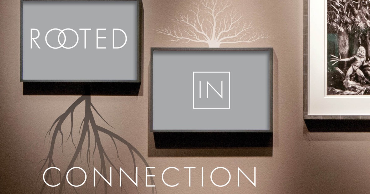 Two framed gray panels on a wall display the words "ROOTED" and "IN" with tree roots and branches extending from the frames, accompanied by the word "CONNECTION" below.
