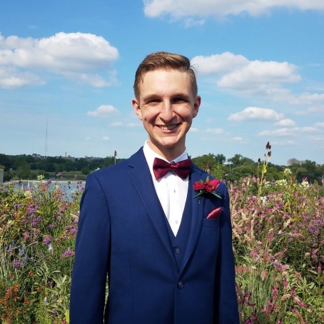 Joe Beggs in blue suit with red bow tie standing in front of garden