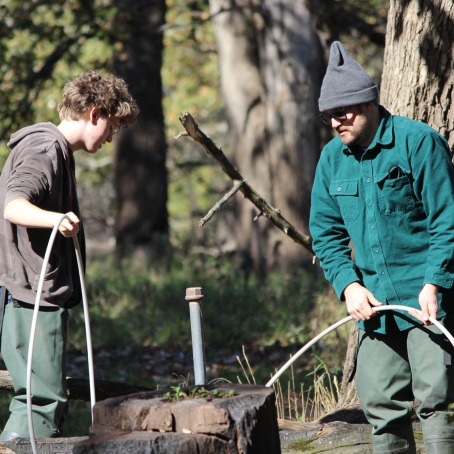 Andrew Graham and Seth Van Helten sampling groundwater near a capped pipe and stump