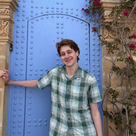a person smiles for a photo while standing in front of a blue metal door