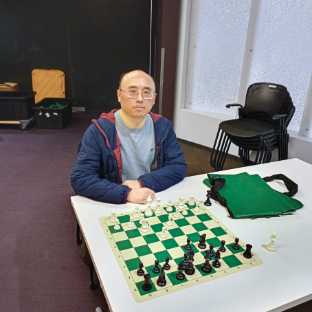 Charlie Wong playing chess set on a green and white checked cloth