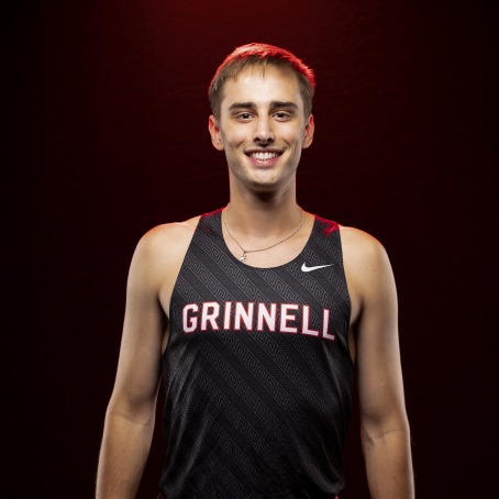 a man wears a black Grinnell College running singlet against a black backdrop