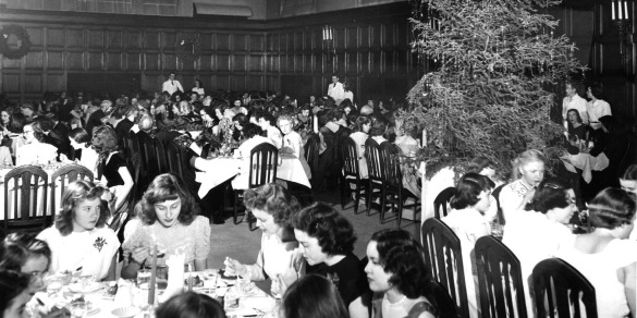 Black and white vintage photo showing women in long dresses enjoying a dinner in Main Hall under a huge Christmas tree