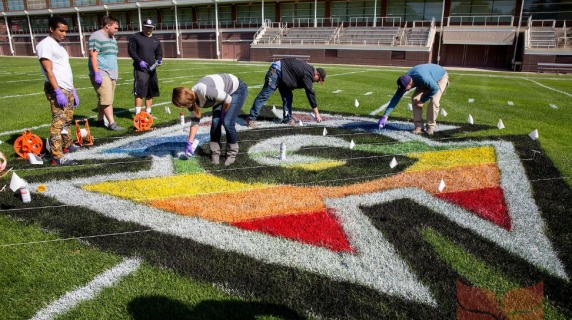 Students painting the football field with the Pride Honor G