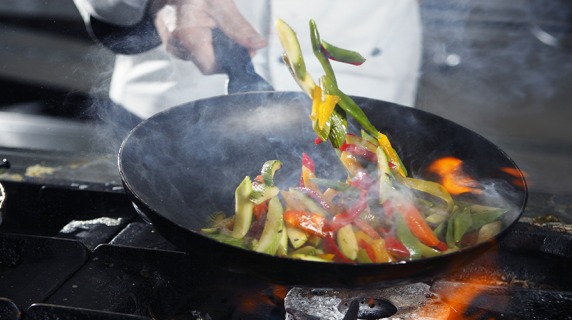 Vegetables being tossed in a skillet over a flame on a stove