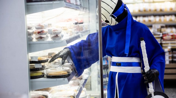 Person in blue suit getting food from food case in grocery store