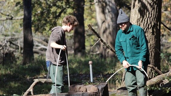 Andrew Graham and Seth Van Helten sampling groundwater near a capped pipe and stump