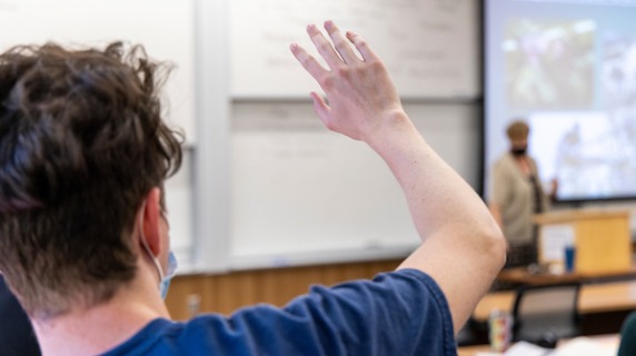 Student has hand raised in a classroom, viewed from behind