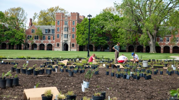 Students in prepared ground planting prairie flora on North Campus with Gates Rawson Tower in the background