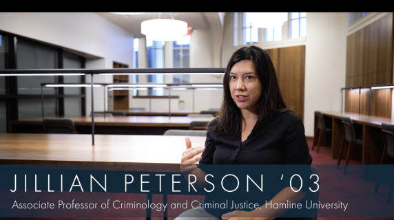 Jillian Peterson '03, Associate Professor of Criminology and Criminal Justice at Hamline University, sits in a reading room in the humanities building. There are many reading tables and well-lit reading lamps behind her.