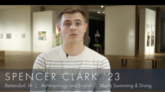 Spencer Clark '23, Anthropology and English major from Bettendorf, IA and a member of Men's Swimming & Diving Team, looks at the camera. Behind him are multiple art pieces from Grinnell College's Museum of Art.