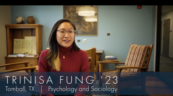 Trinisa Fung '23, a Psychology and Sociology major from Tomball, TX, sits in a well-lit room and looks at the camera. Behind her are wooden chairs and lounge chairs that face each other, a bookshelf, and a piece of art in the wall.