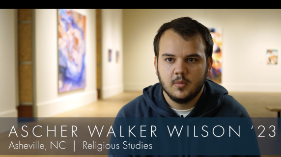 Ascher Walker Wilson '23, a Religious Studies major from Asheville, NC, talks to the camera. Behind him are multiple art displays from the Grinnell College Museum of Art.