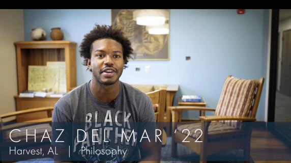 Chaz Del Mar '22, a Philosophy major from Harvest, AL, sits in a well-lit room and warmly talks to the camera. Behind him are three chairs that face each other, a bookshelf with pottery on top, and an art piece.